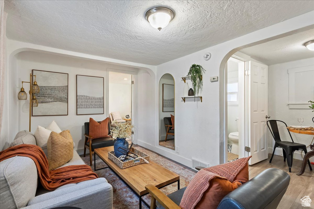 Living area with wood finished floors, a textured ceiling, arched walkways, baseboards, and visible vents