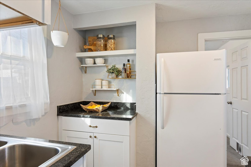 Kitchen featuring open shelves, dark stone countertops, freestanding refrigerator, and white cabinetry