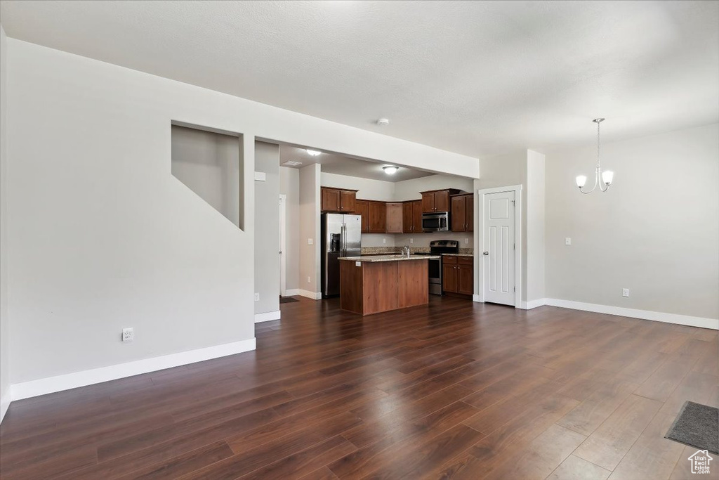 Unfurnished living room with a chandelier, dark wood-style floors, and baseboards