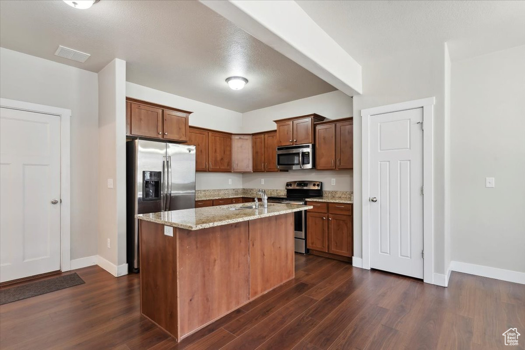 Kitchen with appliances with stainless steel finishes, a sink, dark wood finished floors, and light stone counters