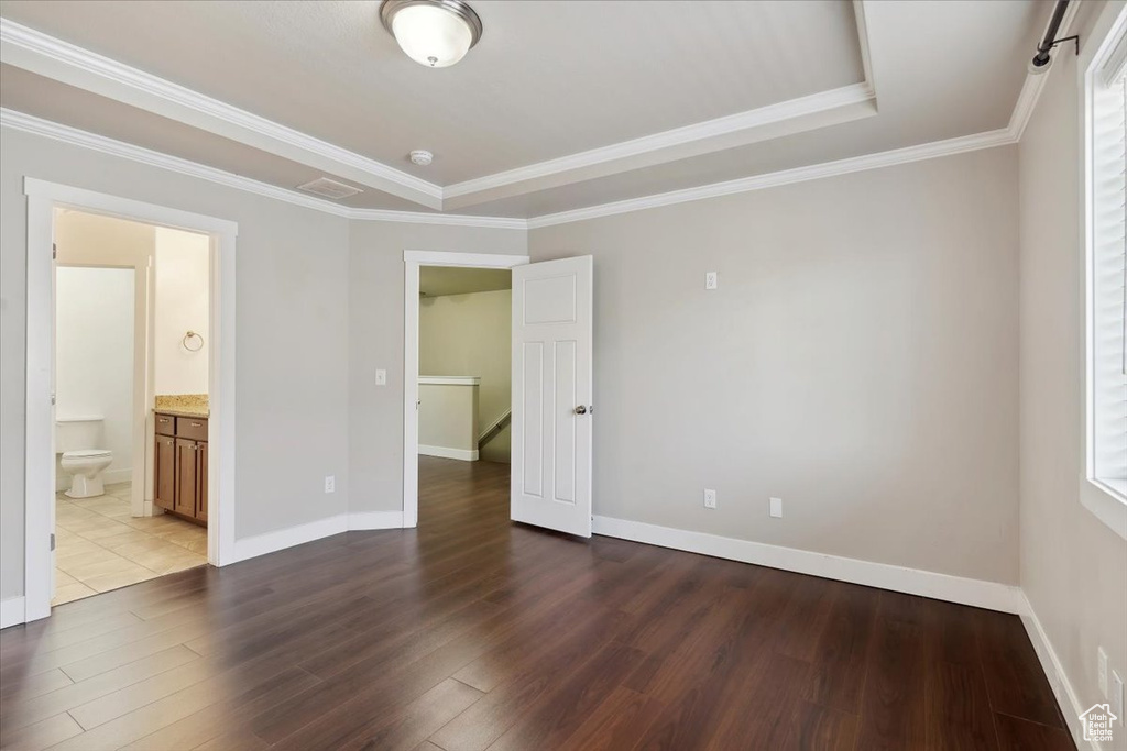 Empty room with wood finished floors, baseboards, ornamental molding, and a raised ceiling