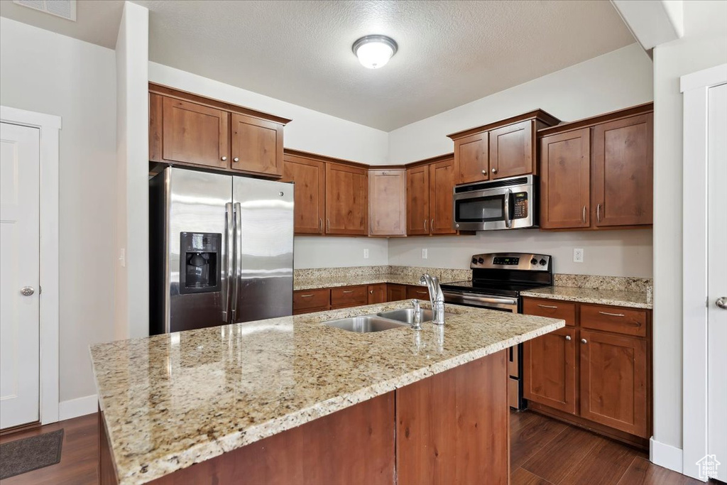 Kitchen featuring stainless steel appliances, a sink, dark wood-style flooring, and light stone countertops