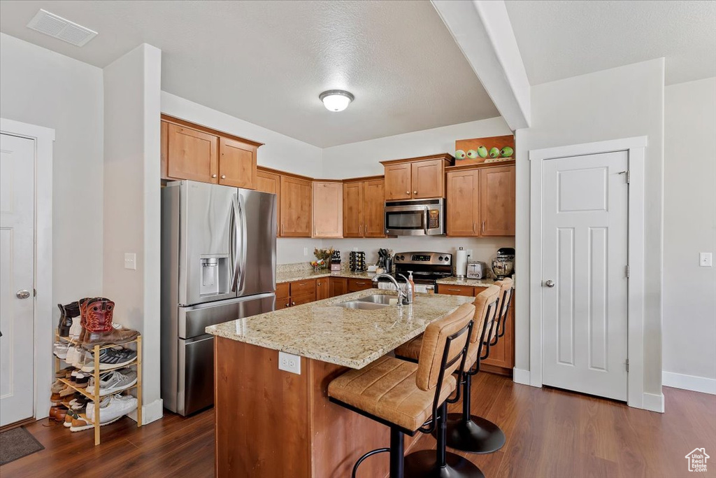 Kitchen featuring appliances with stainless steel finishes, visible vents, light stone countertops, dark wood-type flooring, and a center island with sink