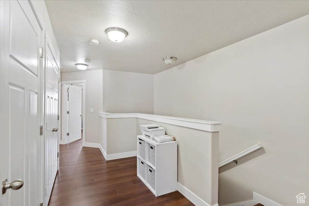 Hallway with baseboards, a textured ceiling, an upstairs landing, and dark wood-style flooring