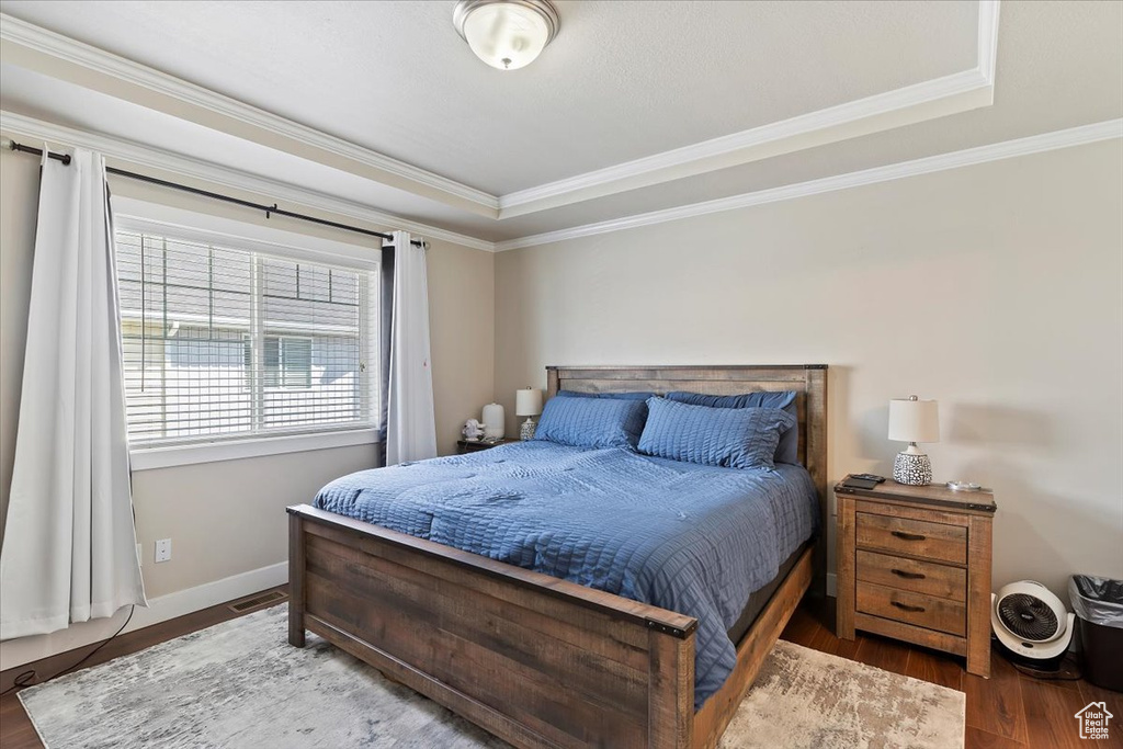 Bedroom with a tray ceiling, crown molding, visible vents, baseboards, and wood finished floors