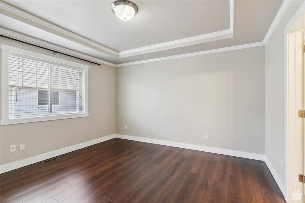Unfurnished room featuring a tray ceiling, dark wood-type flooring, baseboards, and crown molding