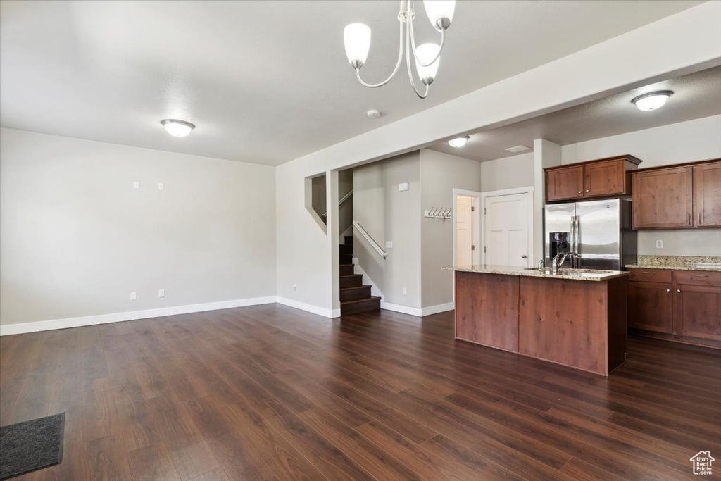 Kitchen with stainless steel fridge with ice dispenser, dark wood-style floors, a chandelier, a center island with sink, and baseboards