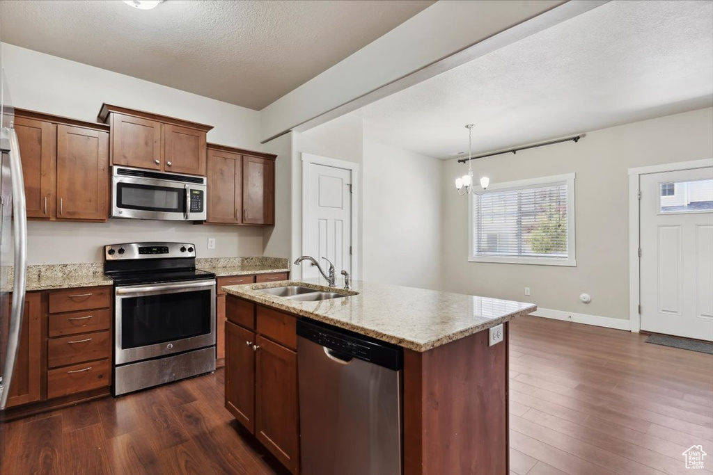 Kitchen featuring stainless steel appliances, dark wood-style floors, a sink, a chandelier, and light stone countertops
