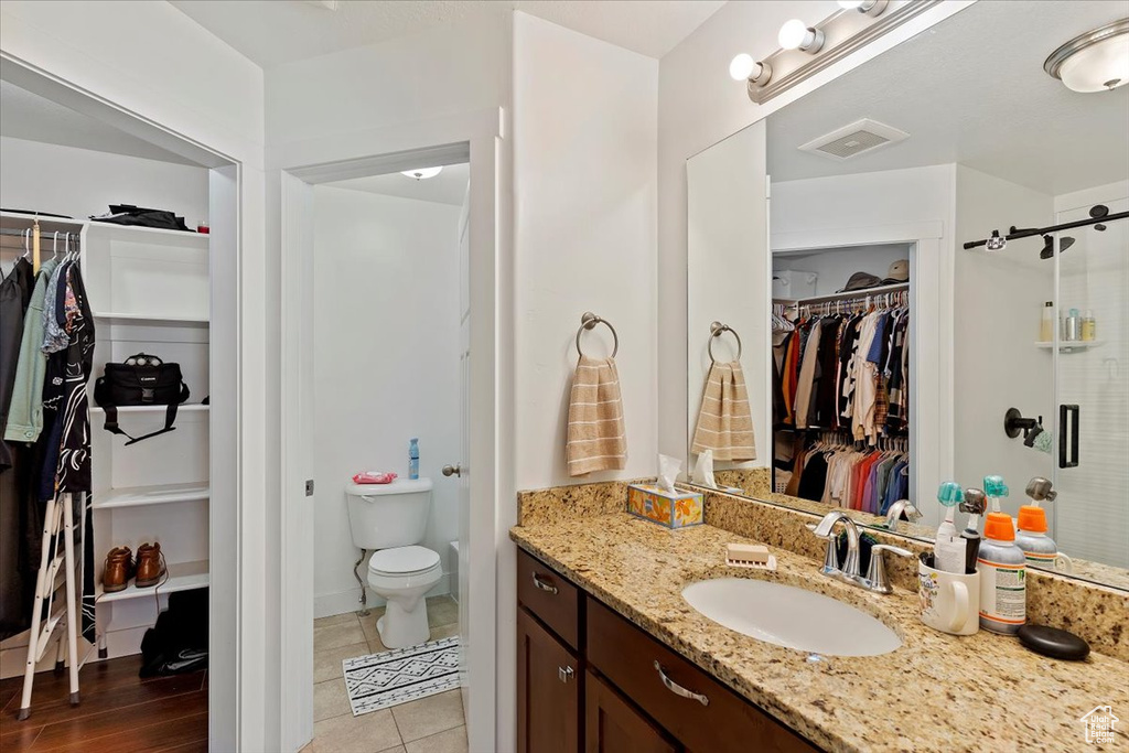Bathroom featuring a shower stall, toilet, vanity, a walk in closet, and visible vents