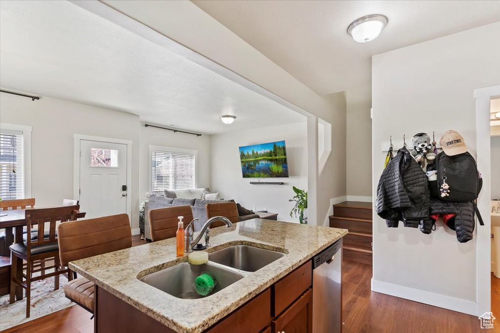 Kitchen featuring a sink, open floor plan, light stone countertops, dishwasher, and dark wood-type flooring