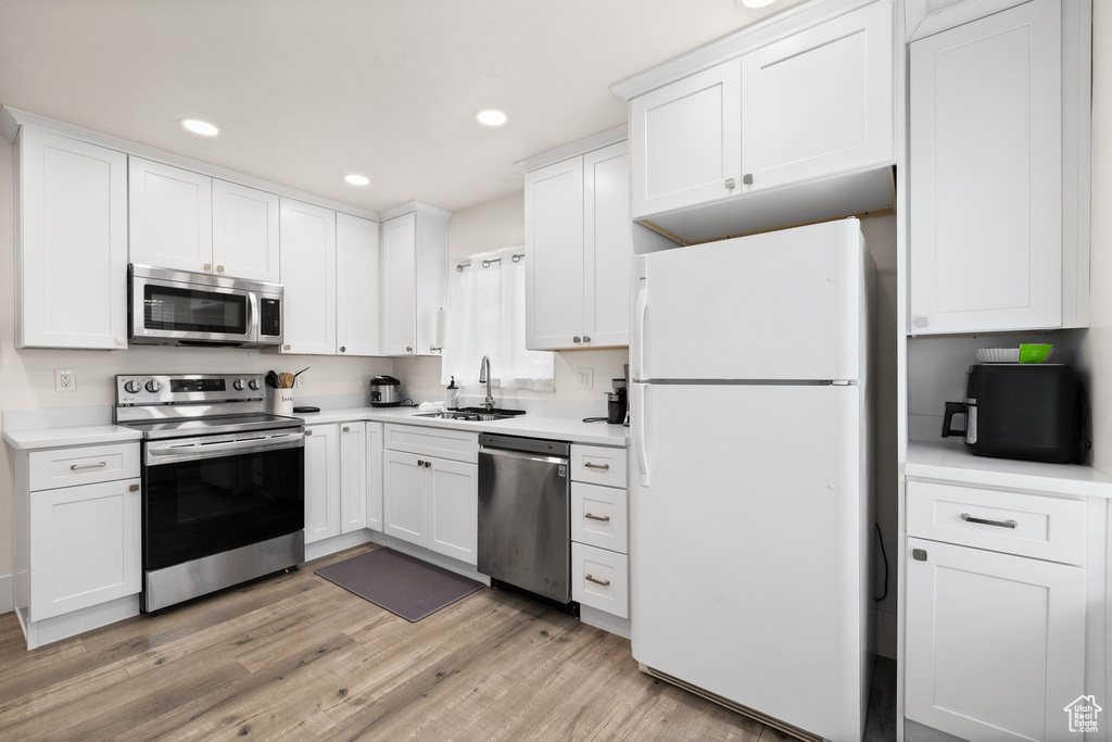 Kitchen with white cabinets, appliances with stainless steel finishes, a sink, light countertops, and recessed lighting