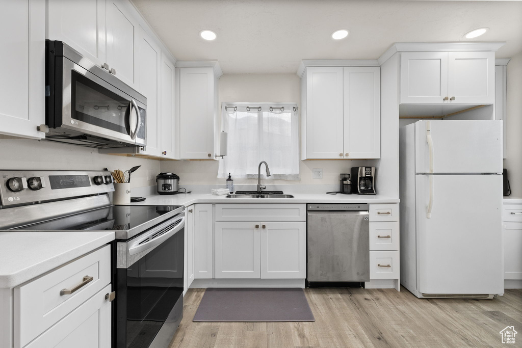 Kitchen featuring light countertops, white cabinetry, a sink, light wood-style flooring, and appliances with stainless steel finishes