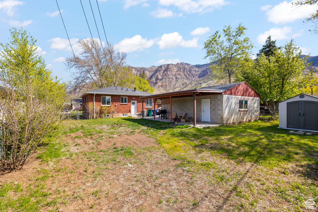 Back of property featuring an outdoor structure, a patio area, a mountain view, and a storage shed