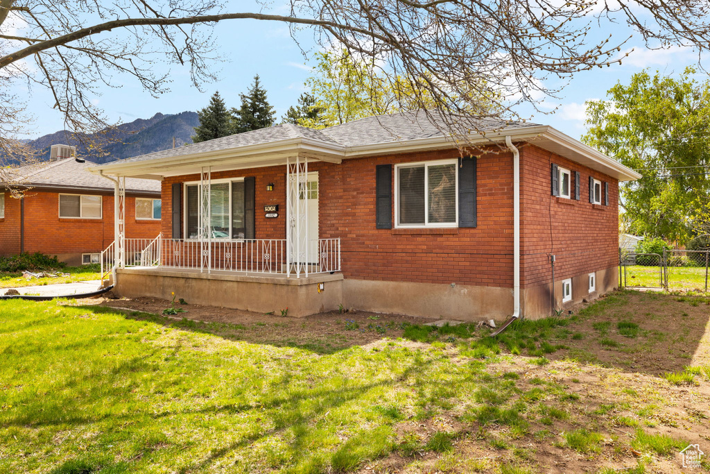 Ranch-style house featuring a porch, brick siding, a mountain view, and a front lawn