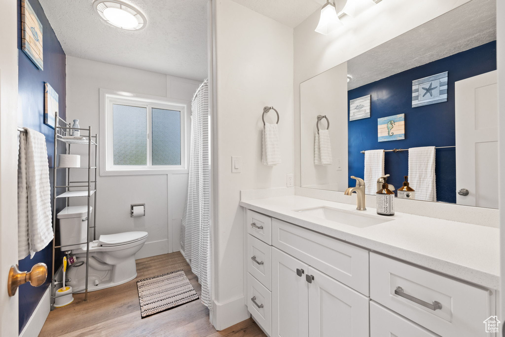 Full bathroom with toilet, a textured ceiling, wood finished floors, and vanity
