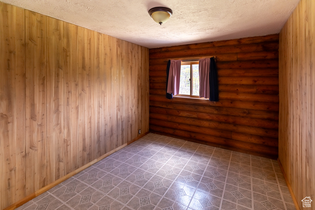 Unfurnished room with a textured ceiling and log walls
