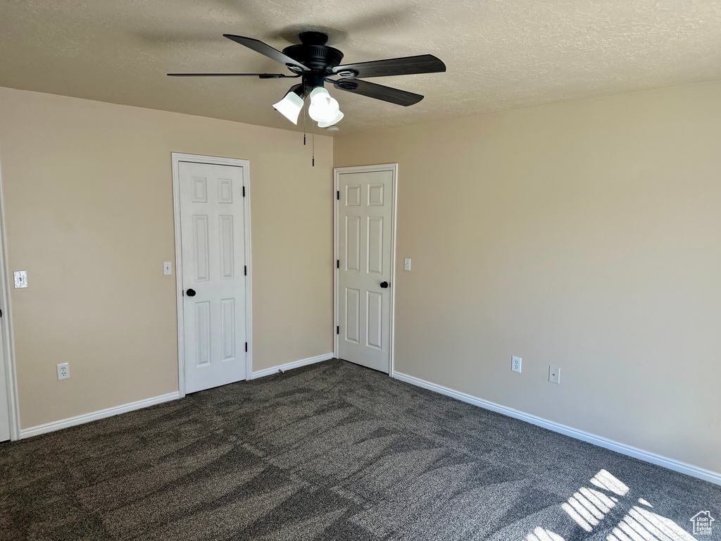 Spare room with dark carpet, a ceiling fan, a textured ceiling, and baseboards