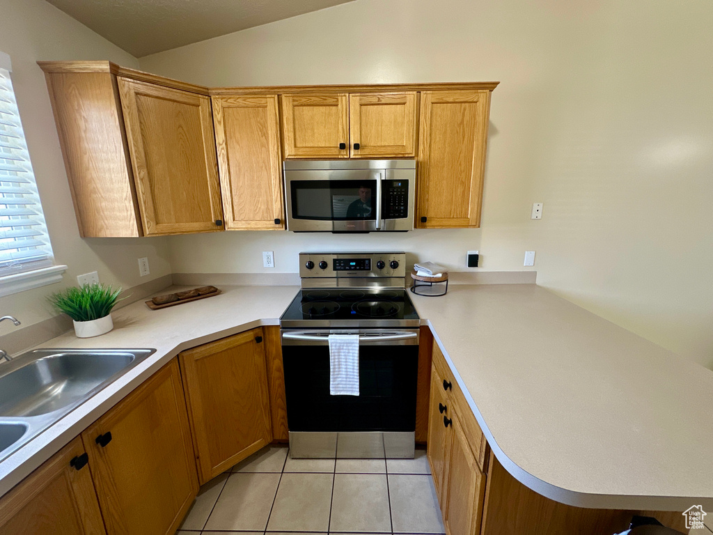 Kitchen featuring light countertops, appliances with stainless steel finishes, a peninsula, and lofted ceiling