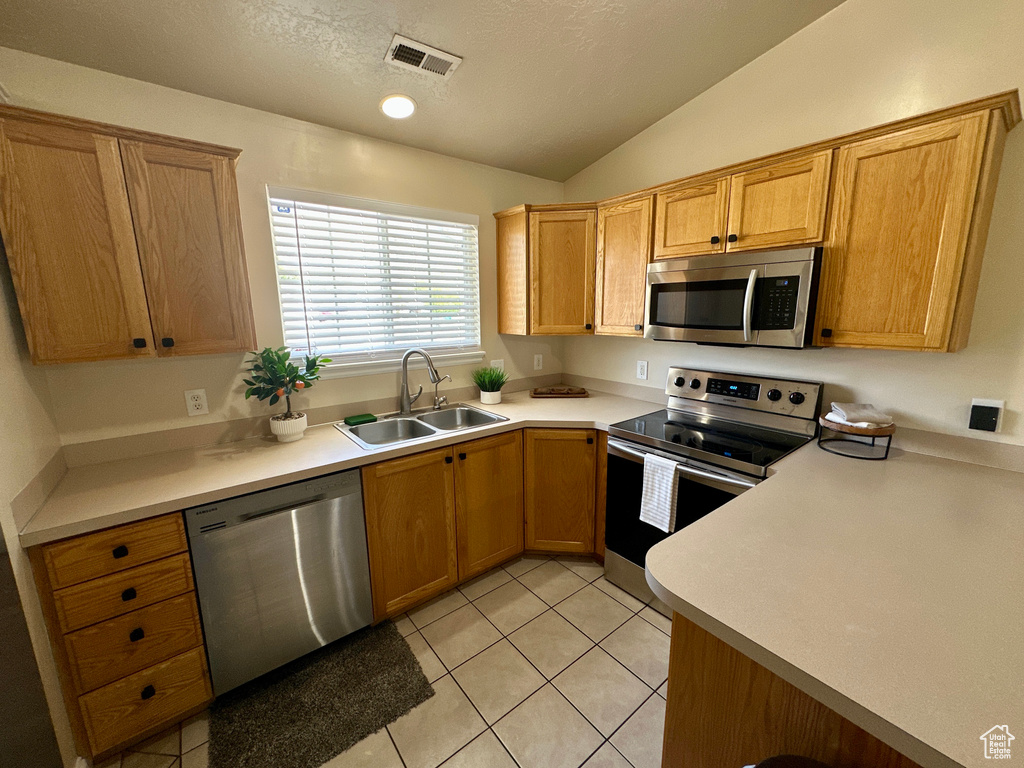 Kitchen with light tile patterned flooring, a sink, stainless steel appliances, vaulted ceiling, and visible vents