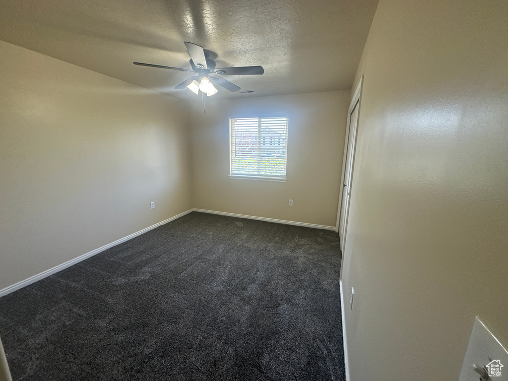Spare room with dark colored carpet, a ceiling fan, baseboards, and a textured ceiling