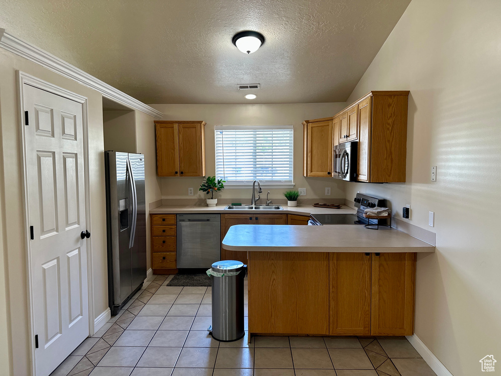 Kitchen with appliances with stainless steel finishes, a sink, a textured ceiling, a peninsula, and visible vents