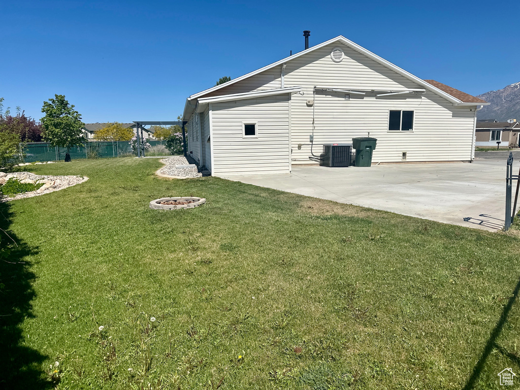 Rear view of property featuring fence, a patio, central AC unit, a lawn, and an outdoor fire pit