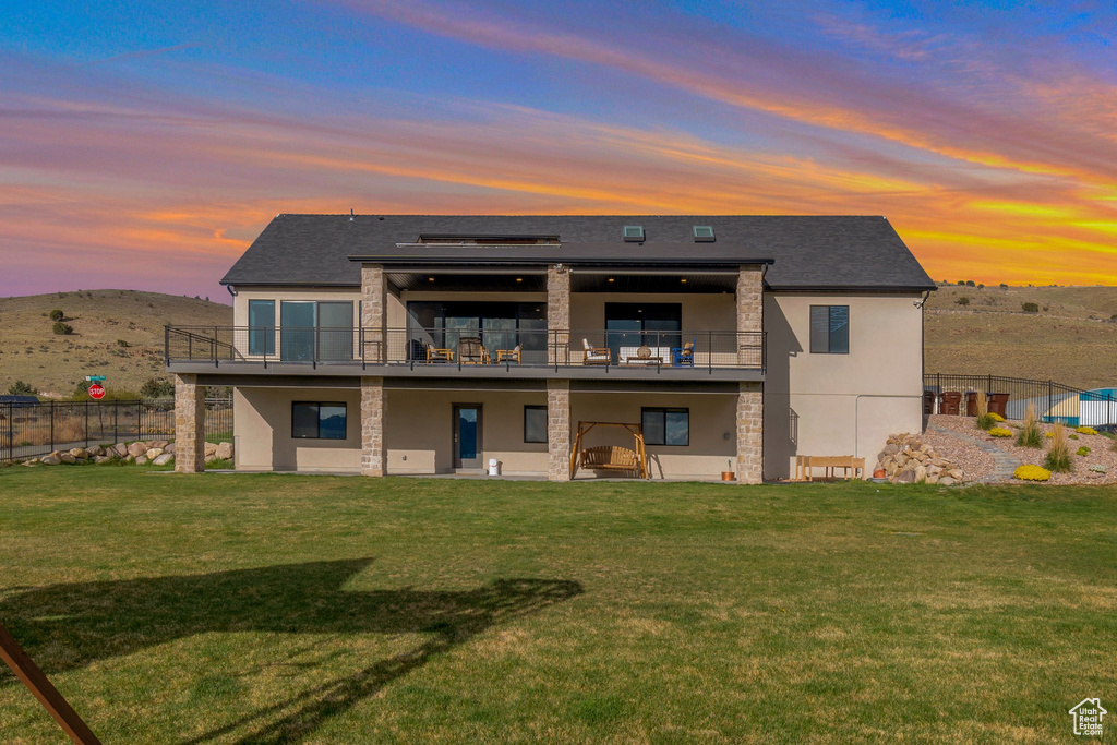 Back of property with stucco siding, a yard, stone siding, and fence