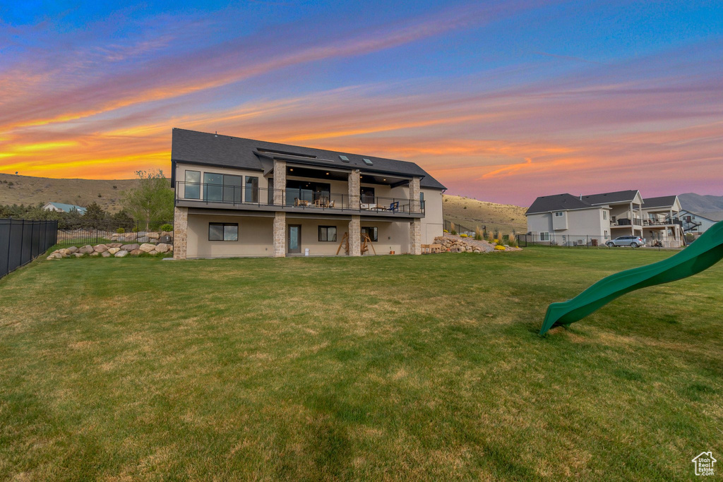 Back of house at dusk featuring a yard and fence