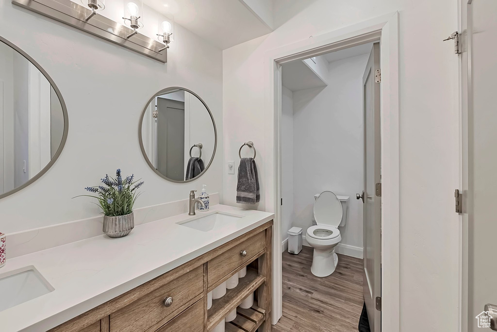 Bathroom with double vanity, a sink, wood finished floors, and toilet