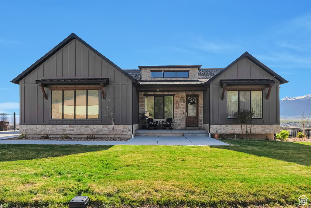 Rear view of house with a shingled roof, board and batten siding, a yard, and stone siding