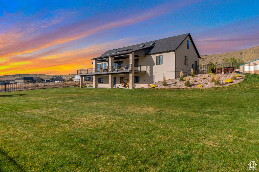 Back of house at dusk featuring a lawn, a wooden deck, stucco siding, and a fenced backyard