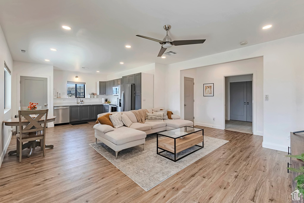 Living room featuring light wood-style floors, baseboards, a ceiling fan, and recessed lighting