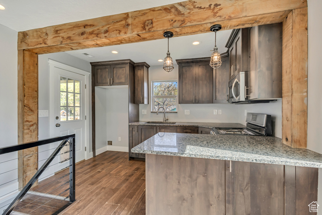 Kitchen featuring dark brown cabinetry, a sink, light stone counters, a peninsula, and stainless steel appliances