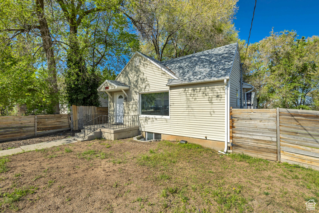 Exterior space with a fenced backyard, roof with shingles, and a front yard