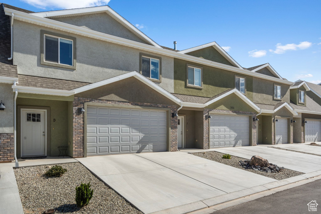 Multi unit property featuring brick siding, an attached garage, driveway, and stucco siding