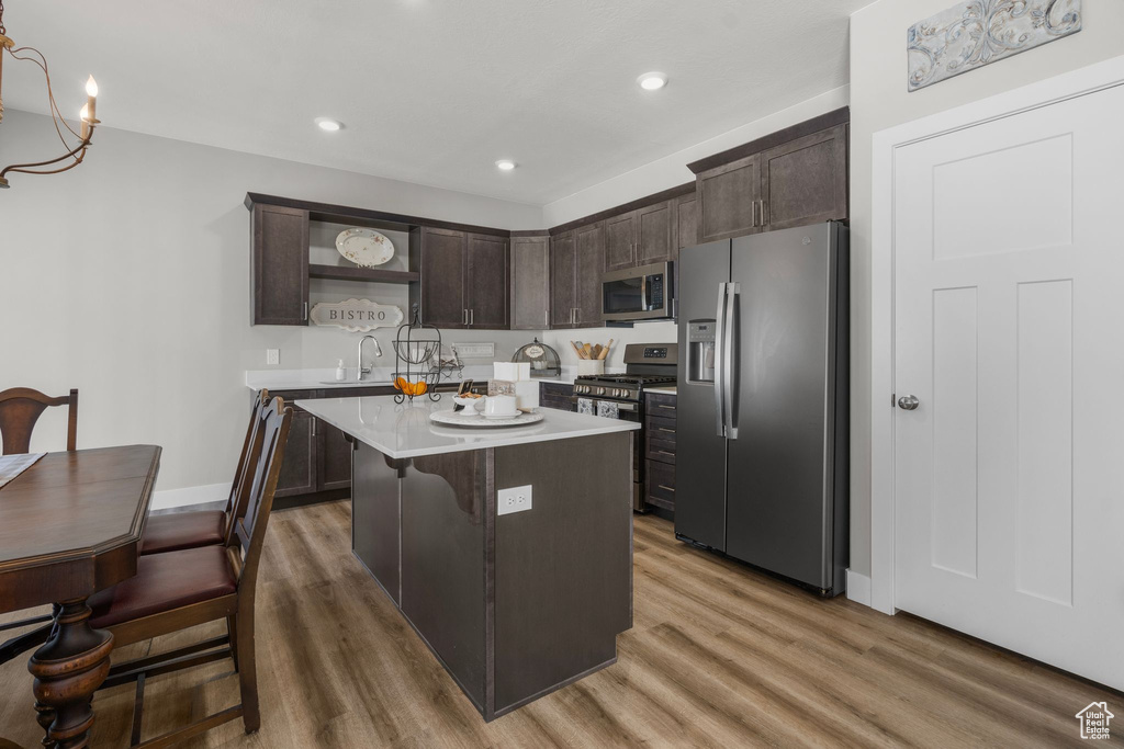 Kitchen with appliances with stainless steel finishes, open shelves, dark brown cabinets, light countertops, and light wood-style flooring