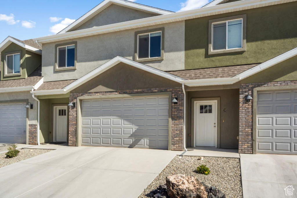 Townhome / multi-family property featuring roof with shingles, an attached garage, brick siding, stucco siding, and concrete driveway