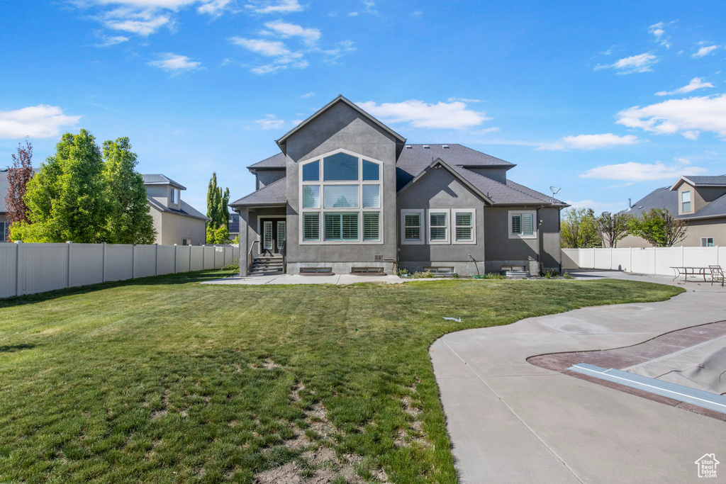Rear view of house with stucco siding, entry steps, a fenced backyard, a lawn, and a patio