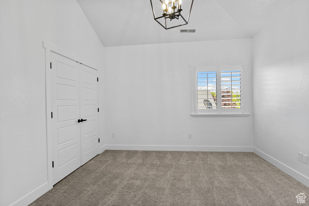 Carpeted spare room with a chandelier, baseboards, visible vents, and vaulted ceiling