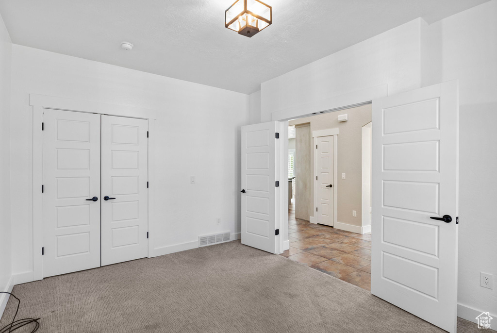 Unfurnished bedroom featuring visible vents, carpet floors, a closet, baseboards, and tile patterned floors
