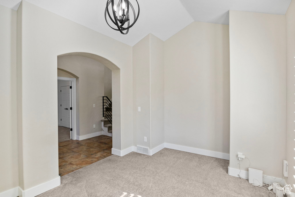 Carpeted empty room with a notable chandelier, arched walkways, baseboards, lofted ceiling, and visible vents