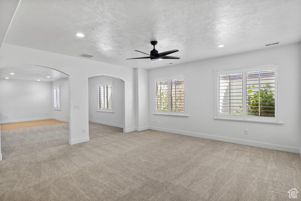 Unfurnished living room with light colored carpet, arched walkways, a textured ceiling, a ceiling fan, and visible vents