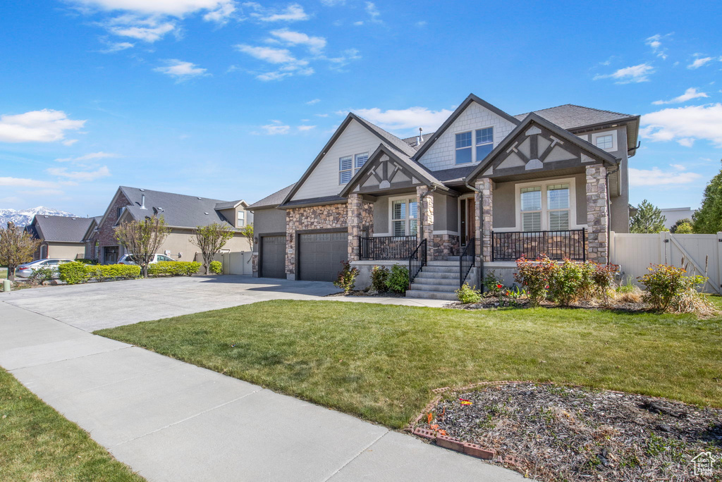 View of front of property featuring a porch, a front yard, concrete driveway, and stone siding