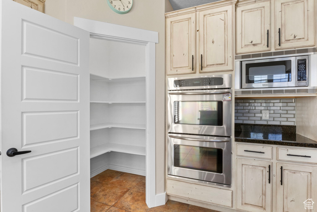 Kitchen featuring dark stone countertops, light brown cabinetry, tasteful backsplash, and stainless steel appliances