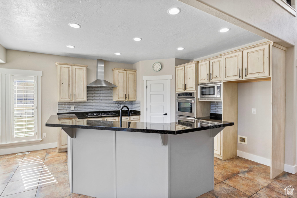 Kitchen with wall chimney range hood, stainless steel appliances, baseboards, and light brown cabinets