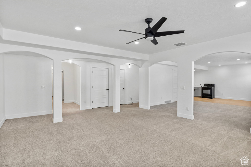 Unfurnished living room with light colored carpet, arched walkways, ceiling fan, and recessed lighting
