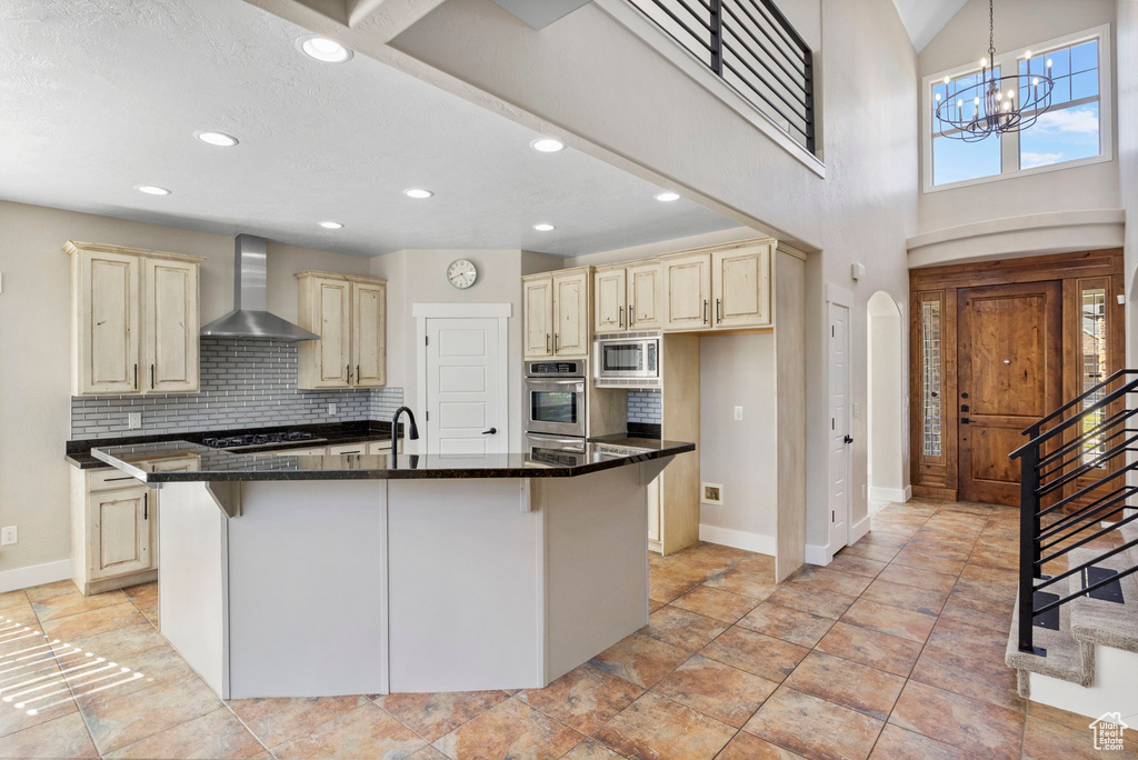 Kitchen featuring appliances with stainless steel finishes, cream cabinets, arched walkways, and wall chimney exhaust hood