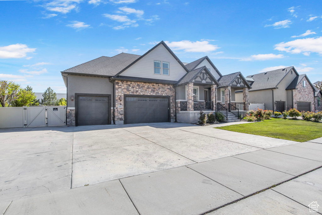 View of front of home with a front lawn, stone siding, a garage, a gate, and driveway