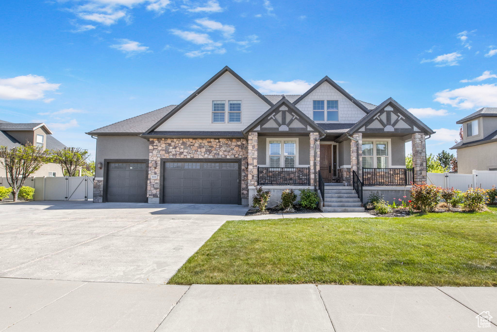 Craftsman-style house featuring fence, stone siding, a front yard, a gate, and covered porch