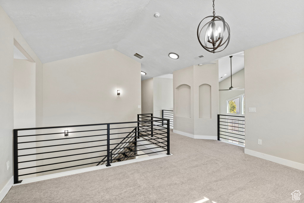 Spare room with an inviting chandelier, carpet flooring, lofted ceiling, and visible vents